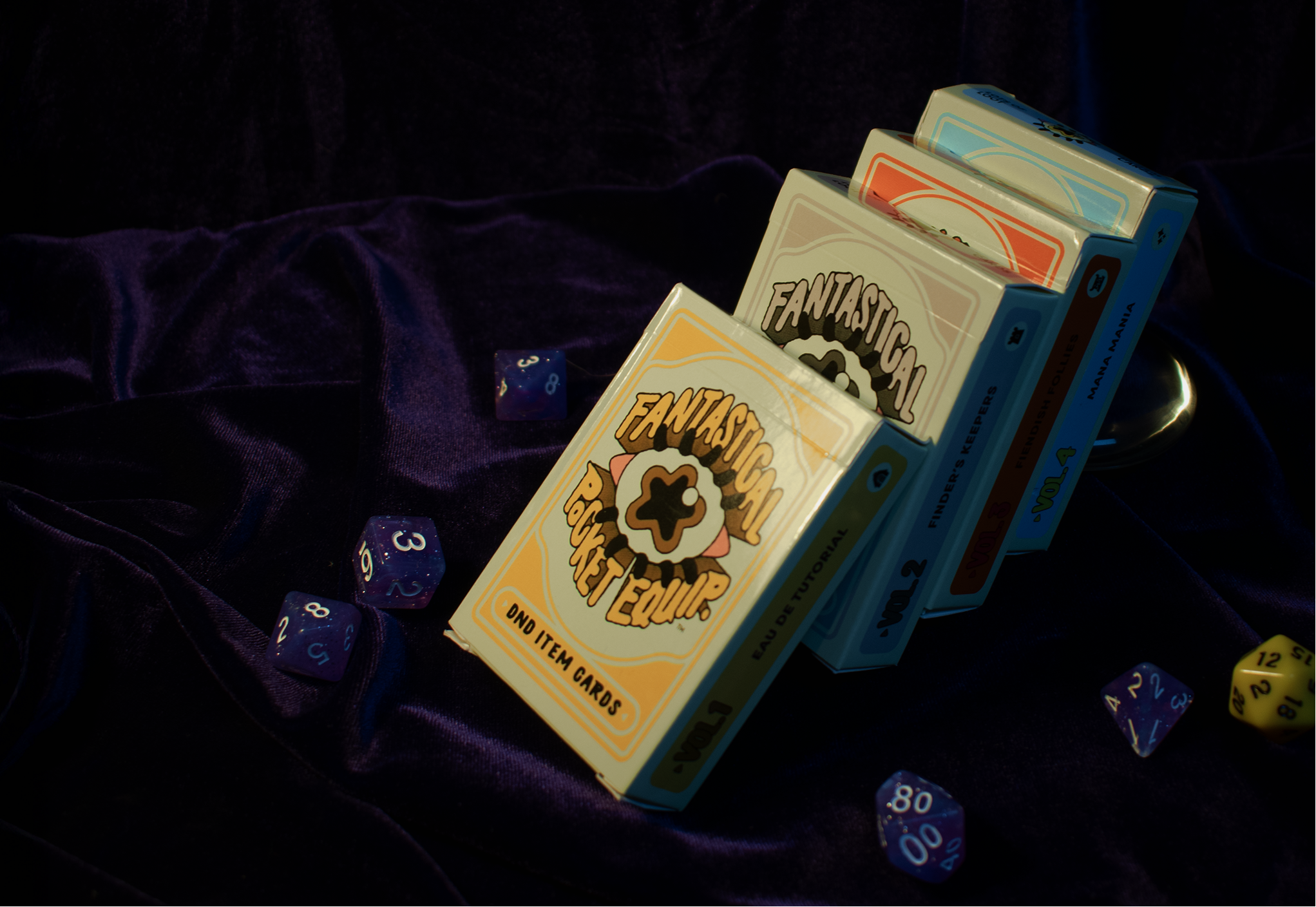 Stack of 'Fantastical Pocket Equipment' item card deck boxes on a dark fabric background with dice around.
